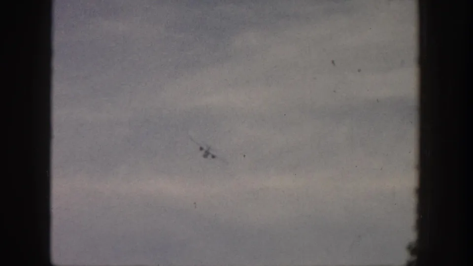 A distant small airplane appears low in the Aspen sky, softened by 1961 8mm grain and faded color.