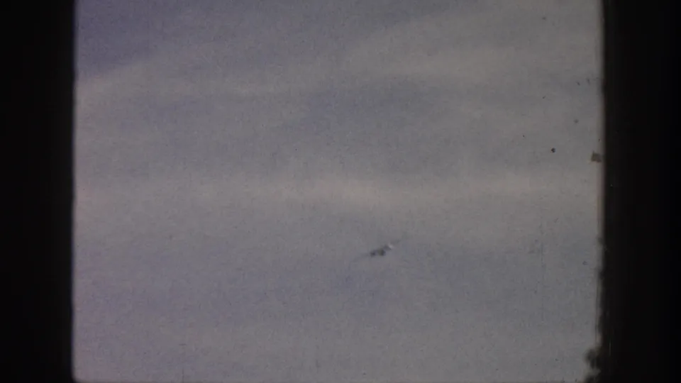 A distant aircraft remains visible as a small dark shape in the 1961 Aspen sky, framed by faded 8mm film texture.
