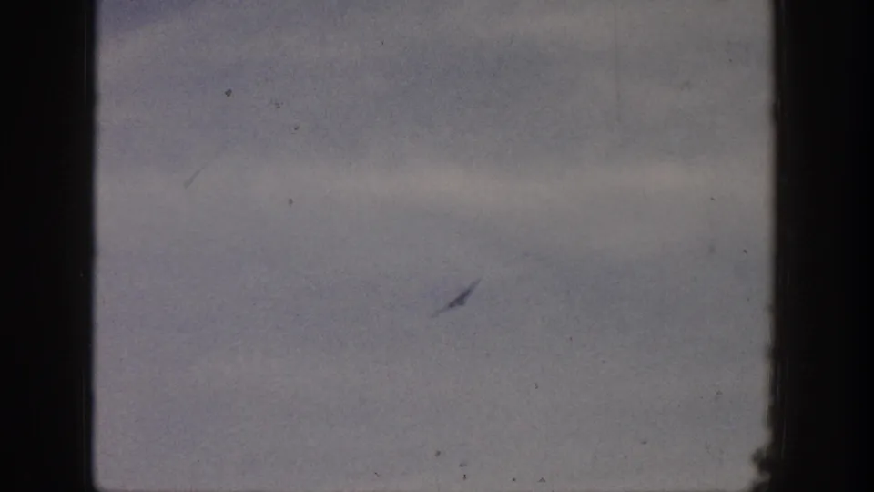 A distant airplane appears faintly in a cloudy sky in supported 1961 Aspen, Colorado 8mm home-movie footage.