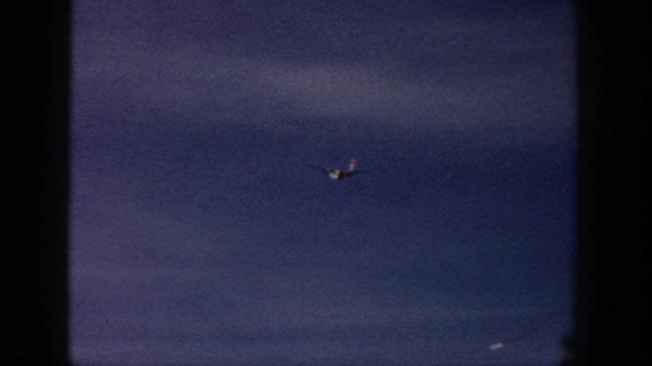 A small airplane crosses a blue-gray cloudy sky in the 1961 Aspen, Colorado home-movie clip.