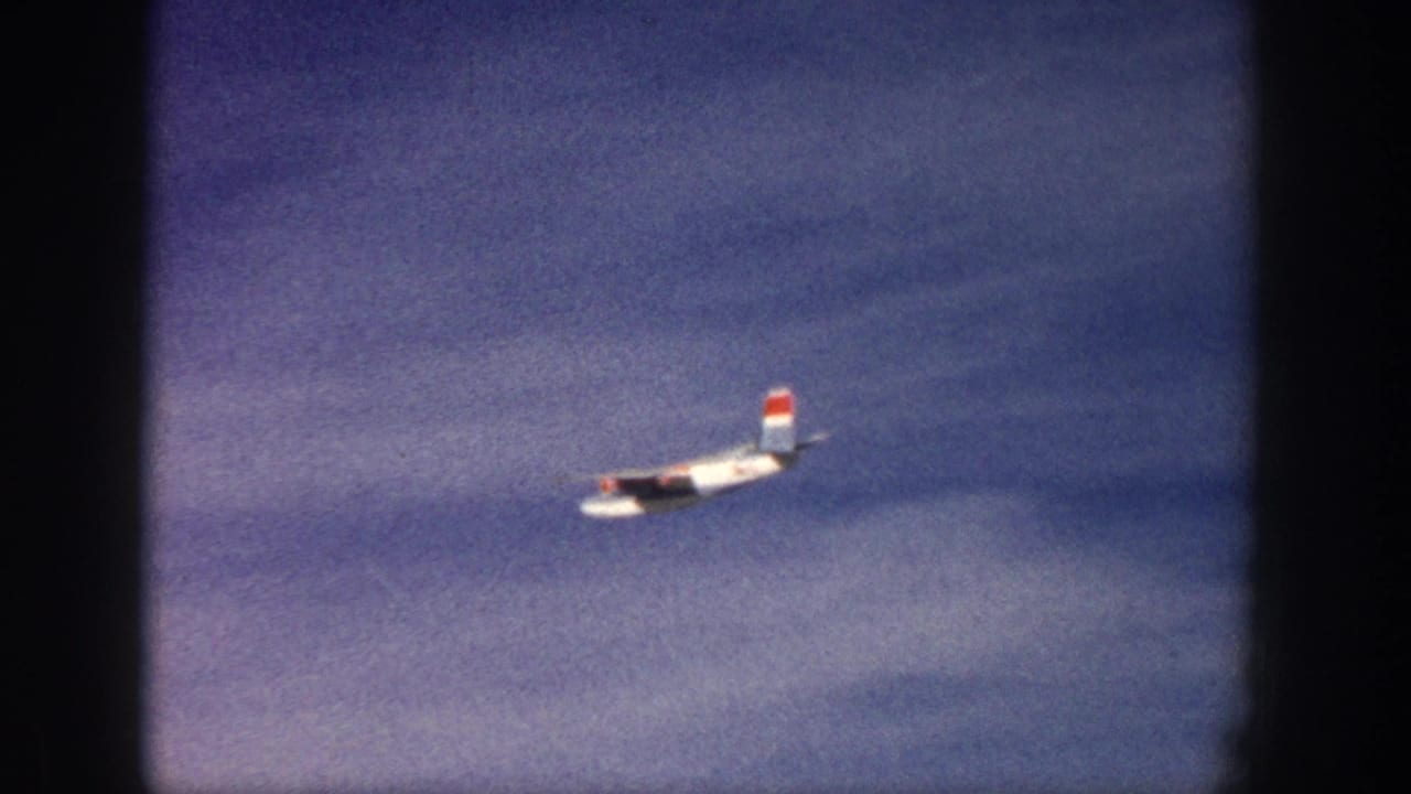 In supplied 1961 Aspen, Colorado footage, a twin-engine propeller plane flies across a blue sky within 8mm frame edges.