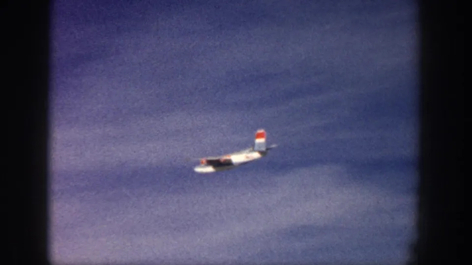 In supplied 1961 Aspen, Colorado footage, a twin-engine propeller plane flies across a blue sky within 8mm frame edges.
