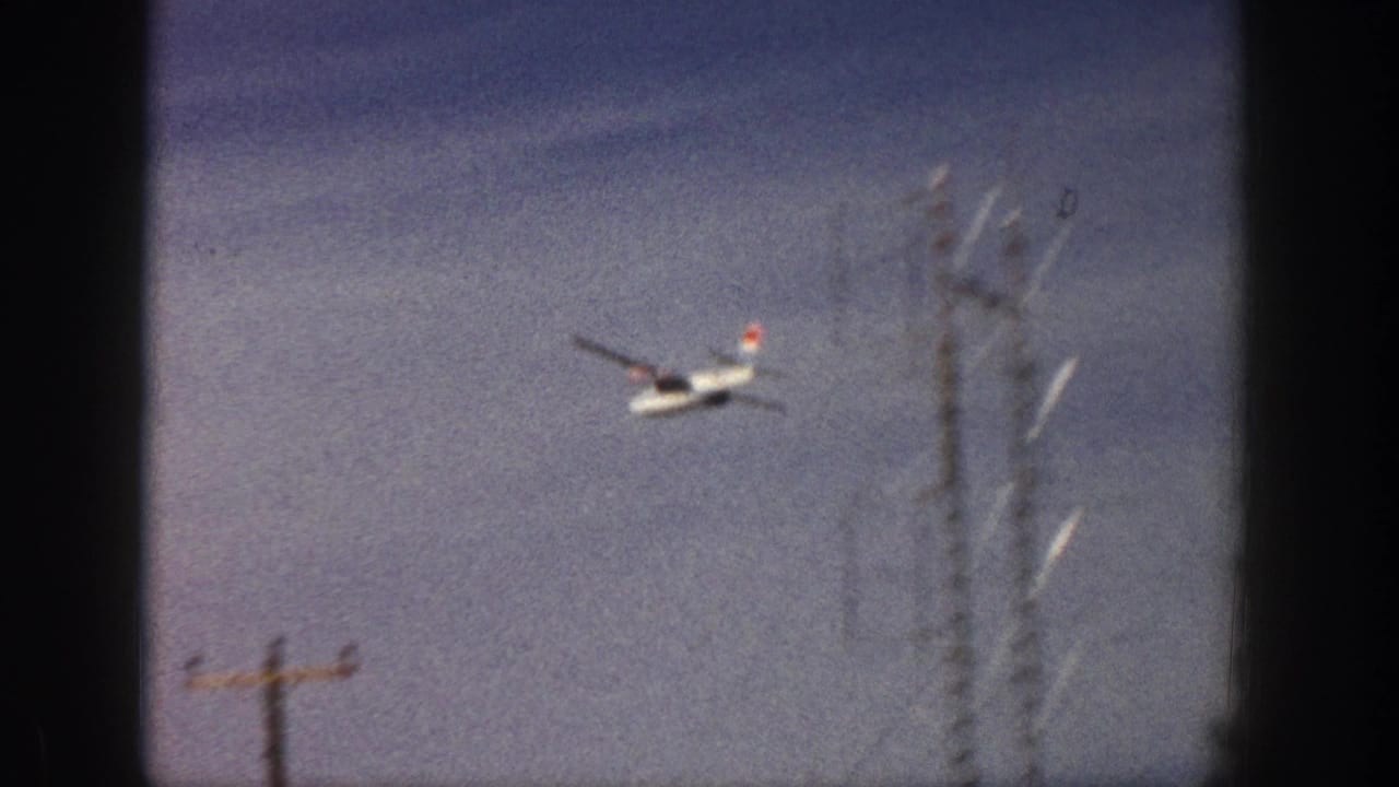 The plane continues across the sky above visible roadside utility poles and a tall communications structure in the Aspen clip.