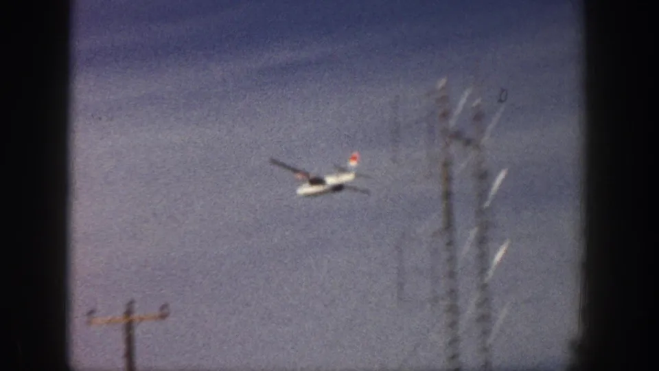 The plane continues across the sky above visible roadside utility poles and a tall communications structure in the Aspen clip.