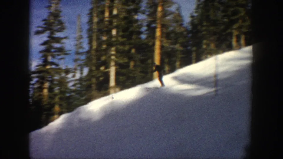 Aspen, Colorado 1961 frame of a skier crossing a sunlit snowy run with evergreens and trail poles behind.