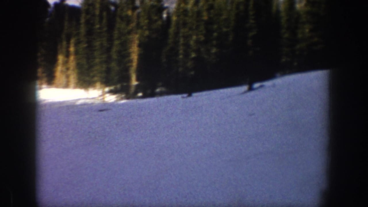 1961 Aspen home-movie frame showing a distant skier crossing a wide snowy slope lined with evergreens.