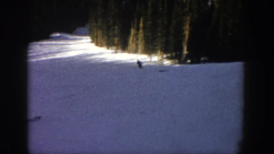 Wide 8mm view of a skier descending a snow-covered Aspen slope near dense evergreen trees.