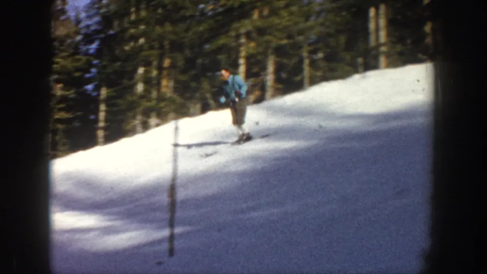 Closer 1961 Aspen frame showing a skier in blue outerwear passing a pole on the snow-covered slope.