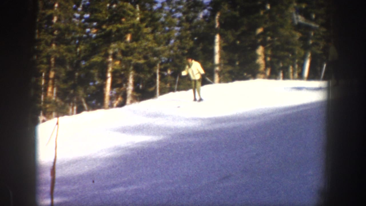 A distant skier in a light jacket appears on a bright snowy rise with trees behind them in 1961 Aspen footage.
