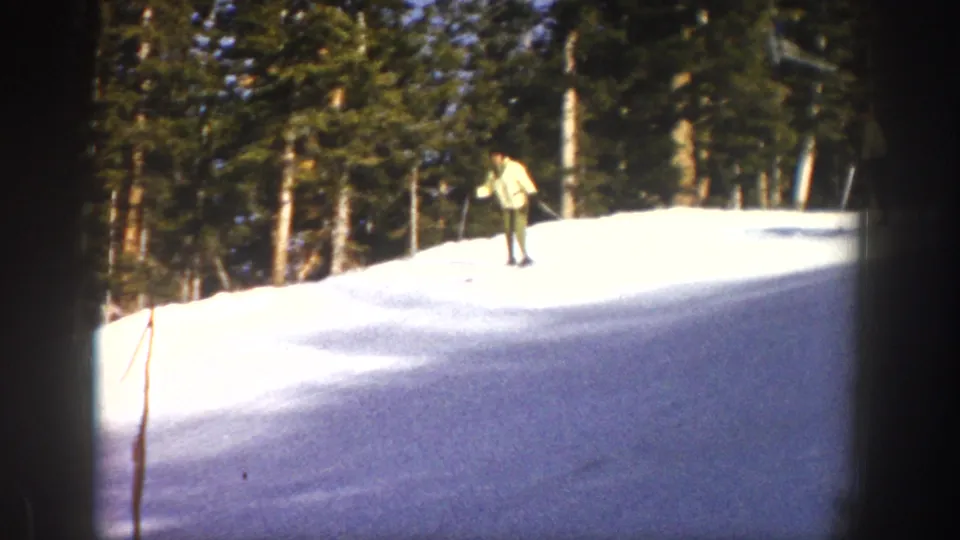 A distant skier in a light jacket appears on a bright snowy rise with trees behind them in 1961 Aspen footage.