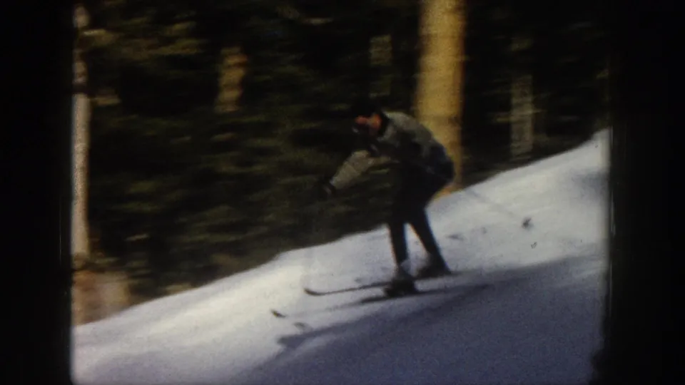 A skier leans into a downhill turn beside the forest edge in this 1961 Aspen 8mm home-movie frame.
