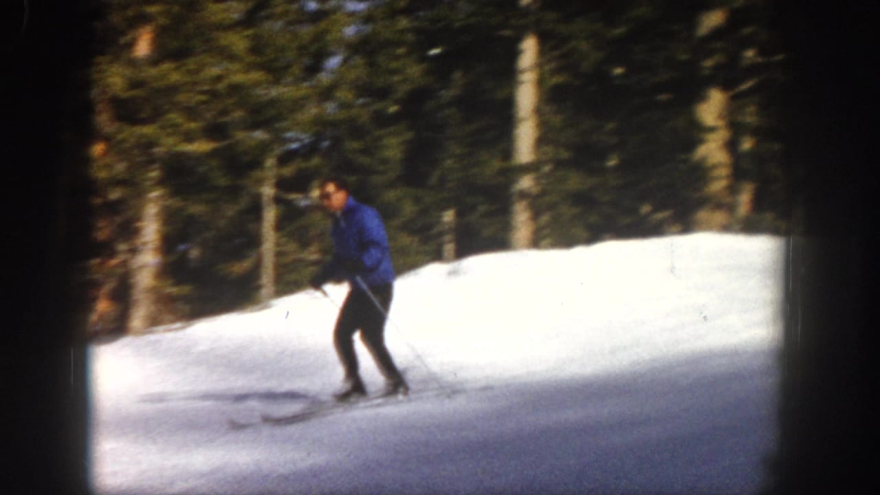A skier in a blue jacket and dark pants moves across a bright Aspen snow slope in 1961 8mm home-movie footage.