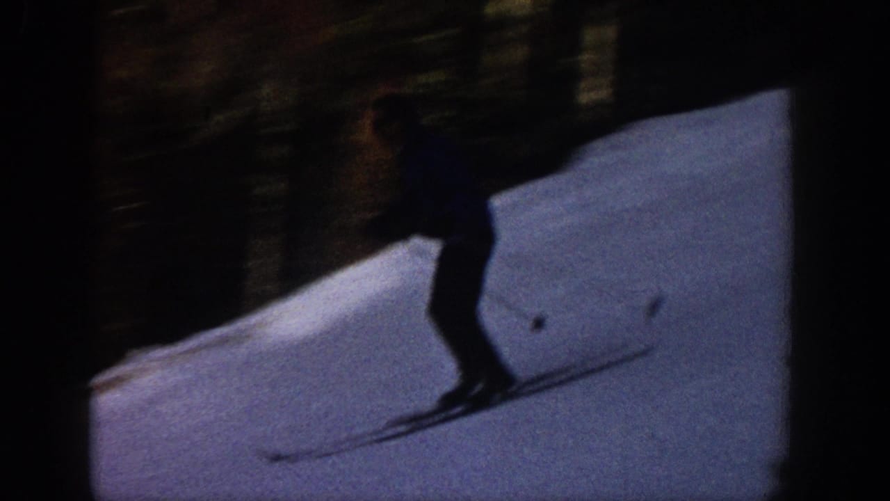 1961 Aspen home-movie frame showing a skier in dark clothing moving downhill across a bright snowy slope.