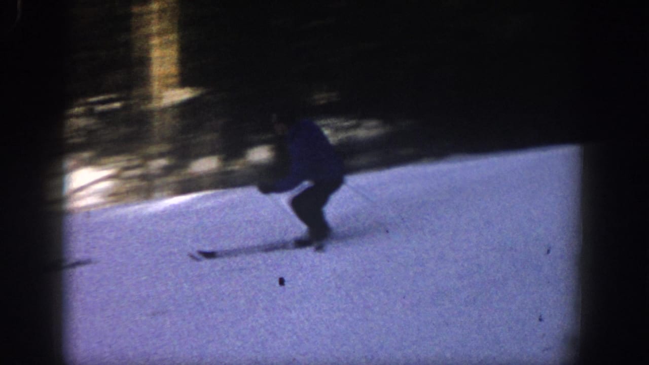Skier crouches while turning on a snowy slope near dark trees.