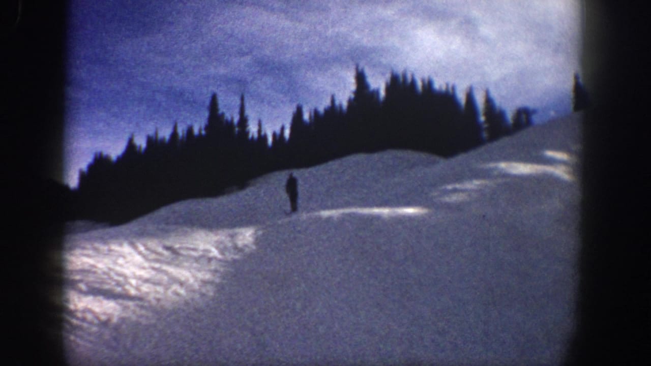 Wide 1961 Aspen home-movie view of a lone skier on a broad snow-covered hillside beneath evergreen trees.