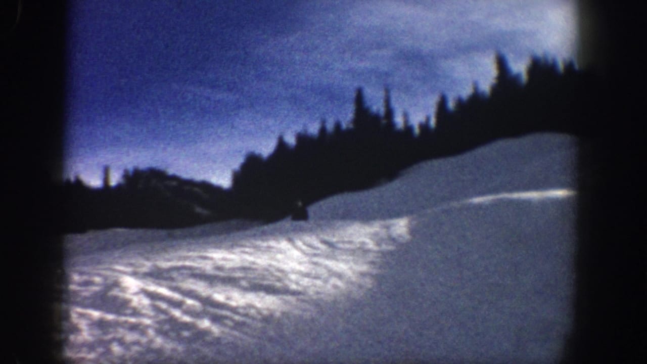End frame from 1961 Aspen footage showing ski tracks on a snowy hillside with a dark evergreen ridge.