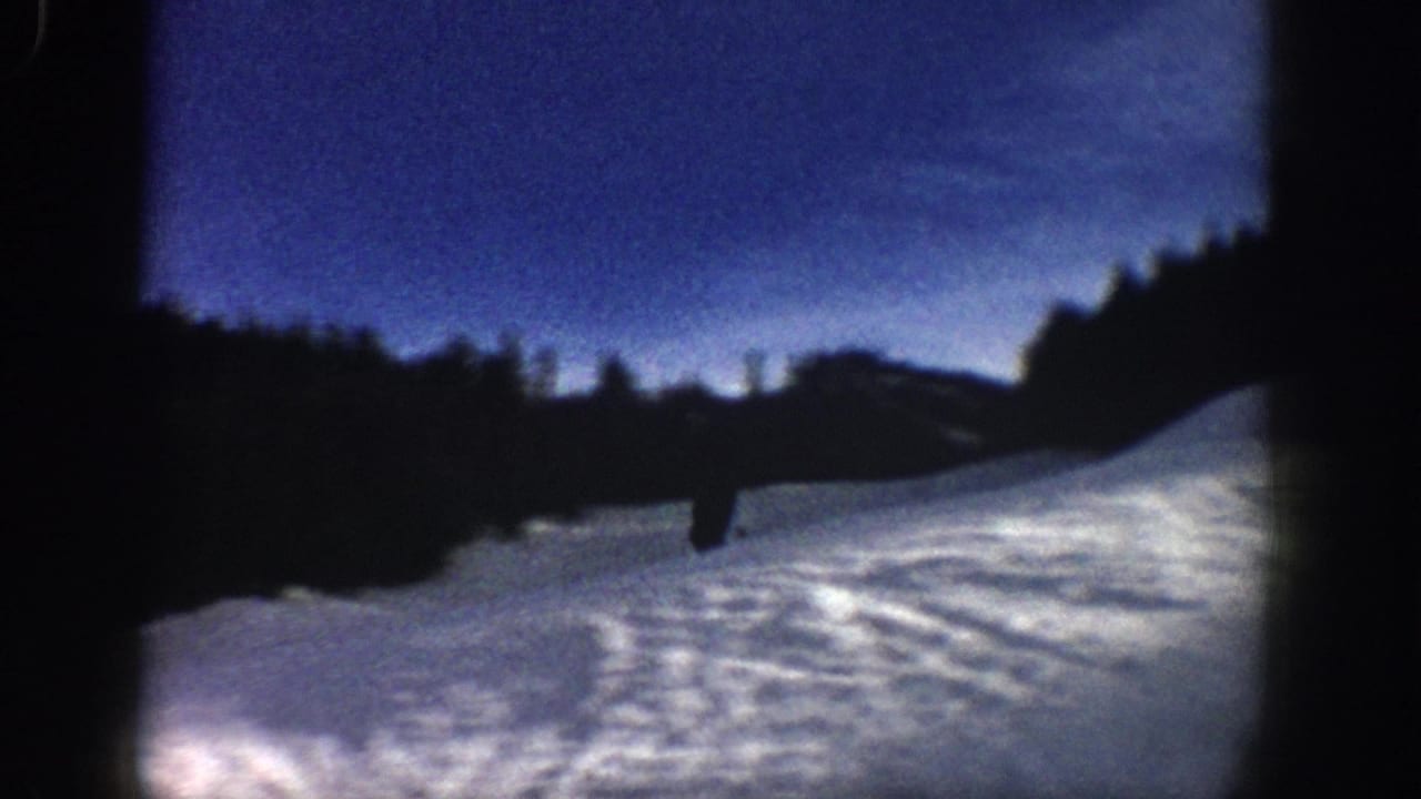 1961 Aspen 8mm frame showing a snow-covered slope under blue dusk sky, with dark tree lines and a small distant figure.