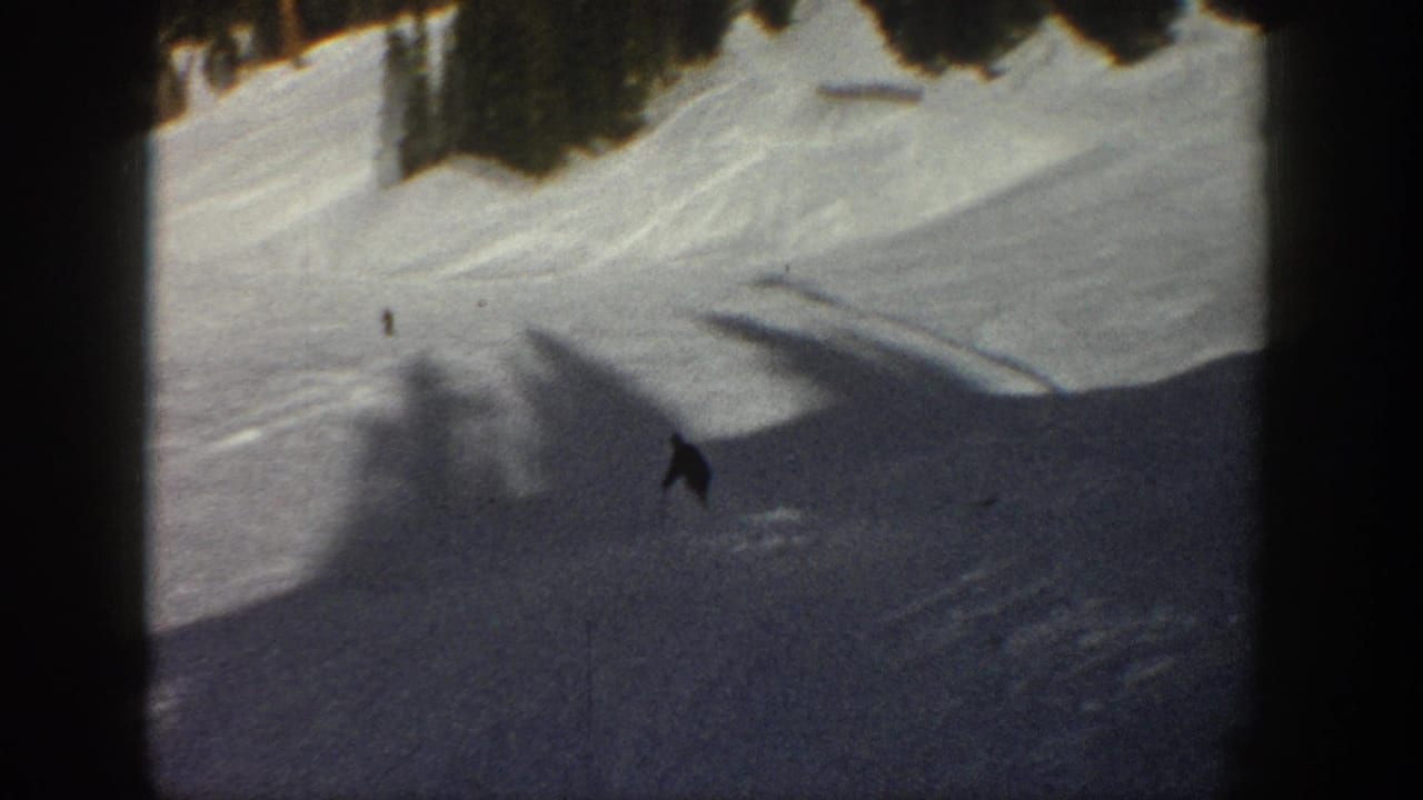 1961 Aspen 8mm frame showing a small skier lower on the slope, surrounded by shadowed snow and dark trees.