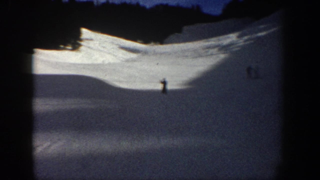 1961 Aspen home-movie frame with a distant skier on a broad snowy slope, dark trees, and blue evening light.
