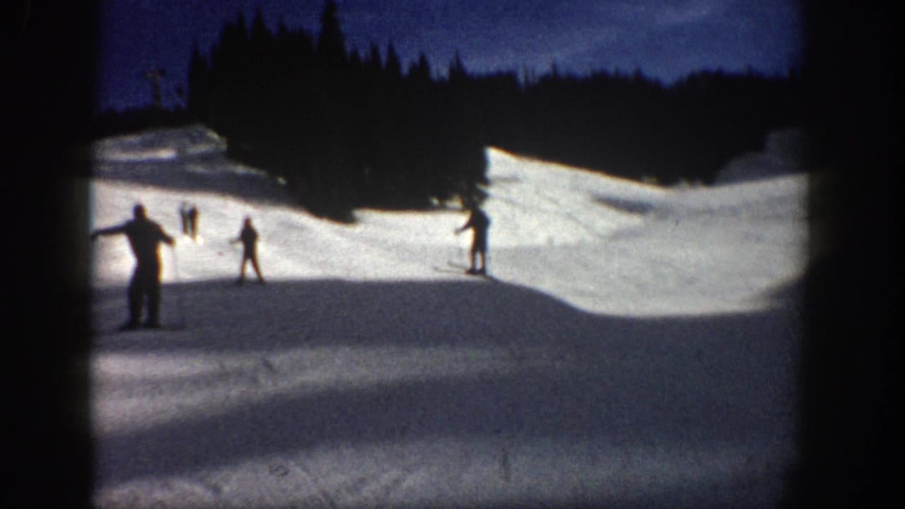 1961 Aspen home-movie frame showing distant skiers on a snowy slope bordered by dark evergreens and a deep blue sky.