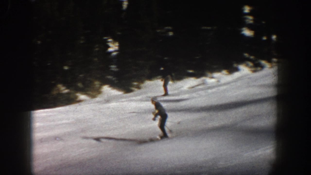 1961 Aspen ski scene with one skier crossing the foreground and another farther uphill near the evergreen border.