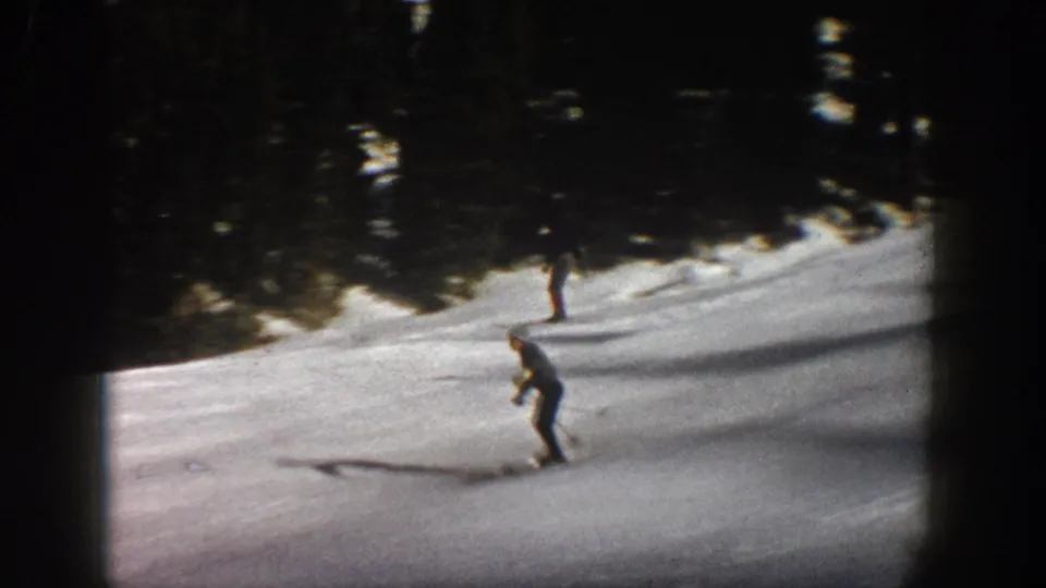 1961 Aspen ski scene with one skier crossing the foreground and another farther uphill near the evergreen border.