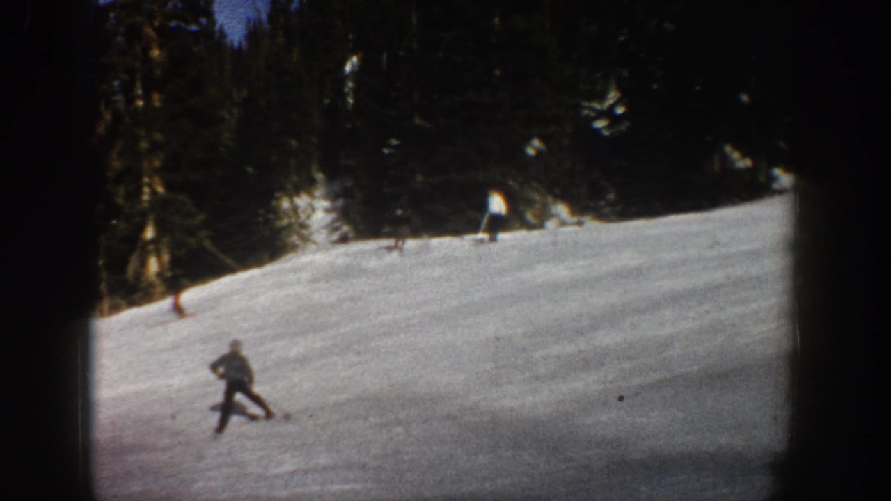 1961 Aspen home-movie frame showing a skier on a snowy slope with dark evergreen trees beyond the run.