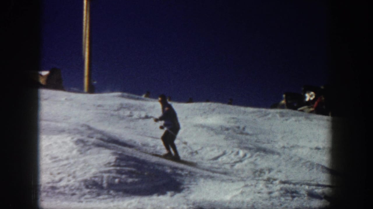 1961 Aspen home-movie frame showing a skier turning on a lit night slope with a pole and dark sky behind.