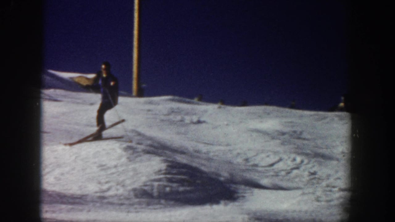 1961 Aspen home-movie frame showing a skier on a snowy slope, with long skis, poles, and dark winter clothing.