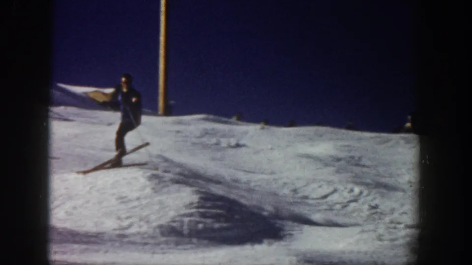 1961 Aspen home-movie frame showing a skier on a snowy slope, with long skis, poles, and dark winter clothing.