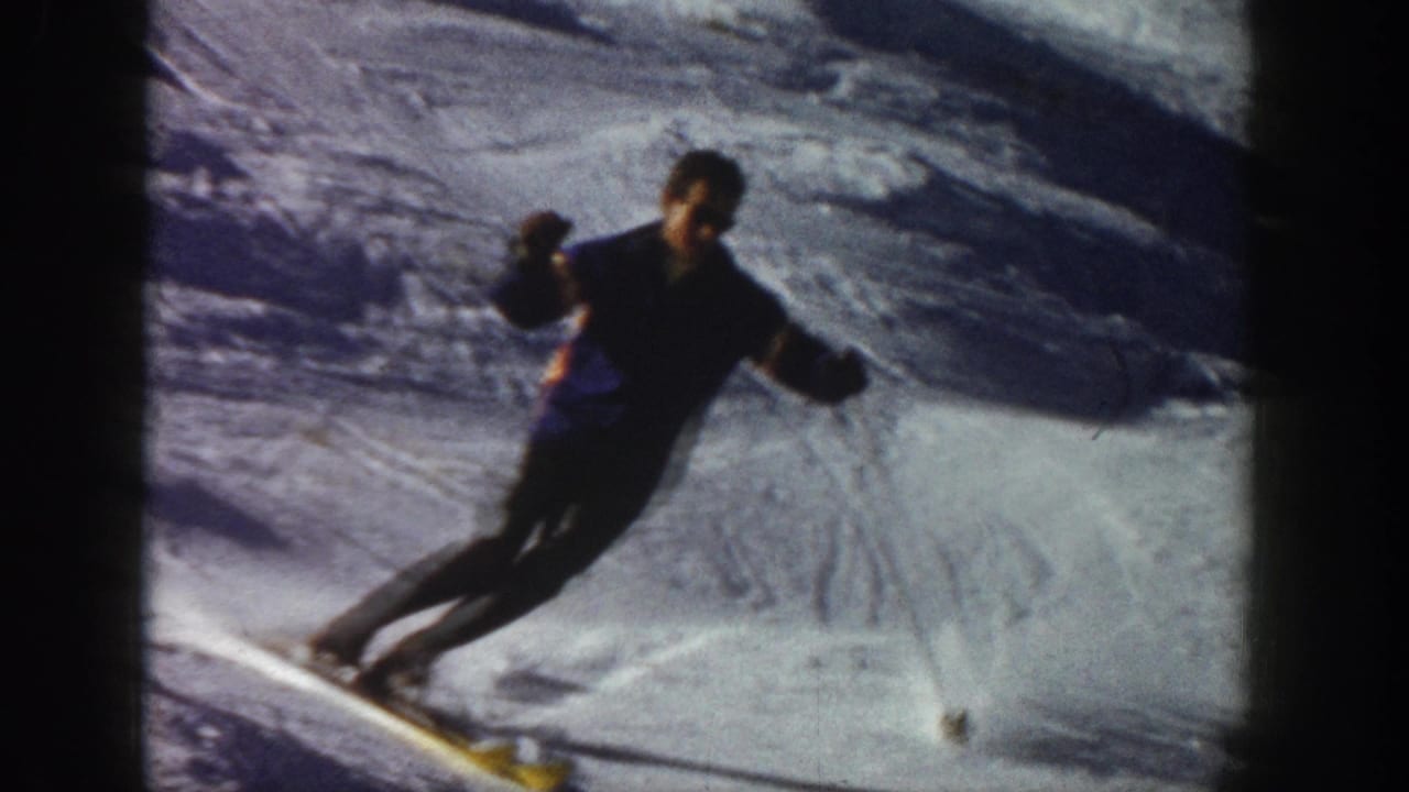 Close 1961 Aspen frame of a skier in dark winter clothing carving downhill across bright, shadowed snow.
