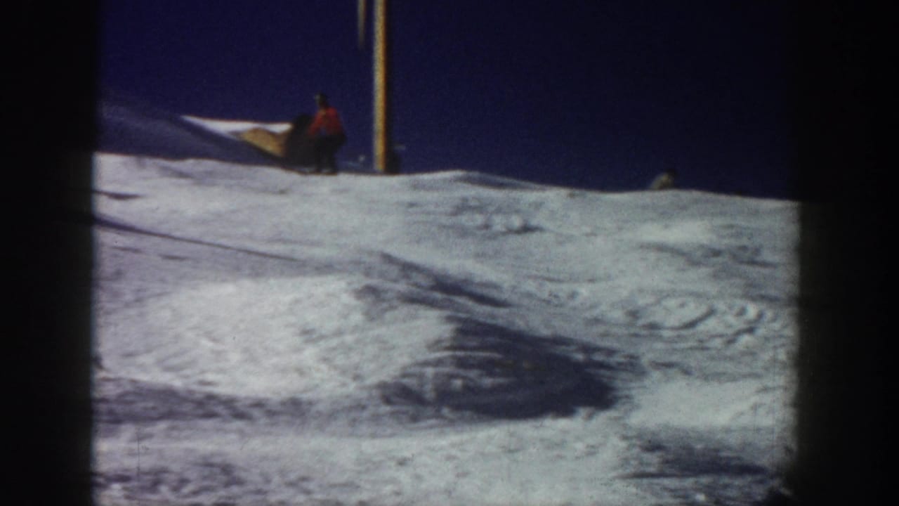 Aspen, Colorado 1961 home-movie frame showing a distant skier in red moving across a snow-covered slope near vertical poles.