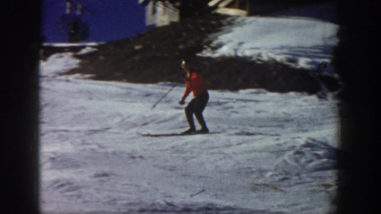 Skier in red jacket gliding across a bright snowy slope.