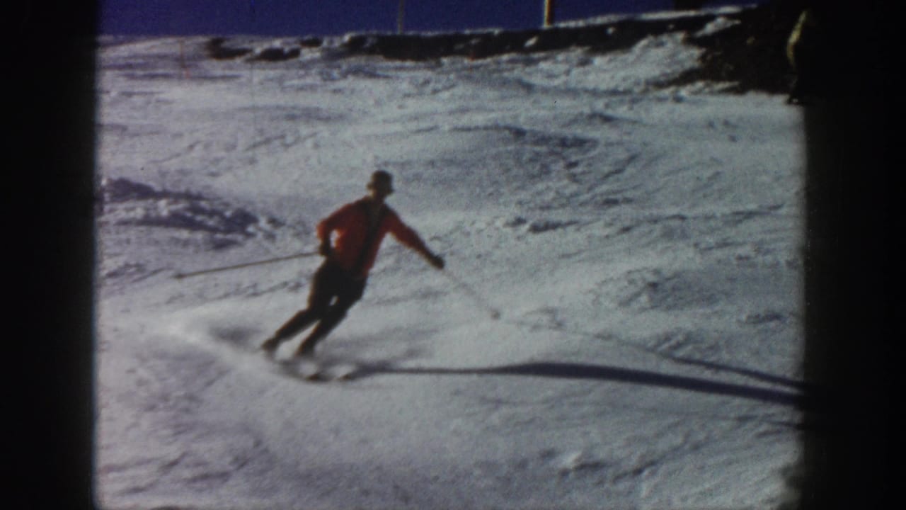 A red-jacketed skier carves downhill on the Aspen snow, with motion blur and a trail of kicked-up snow behind the skis.