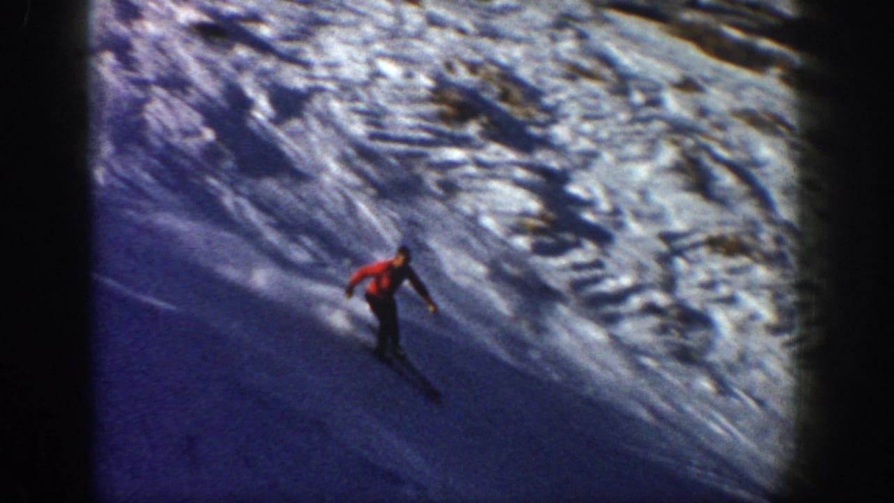 A distant adult skier in red moves down a broad snowy Aspen slope, with textured snow and a long dark shadow visible.