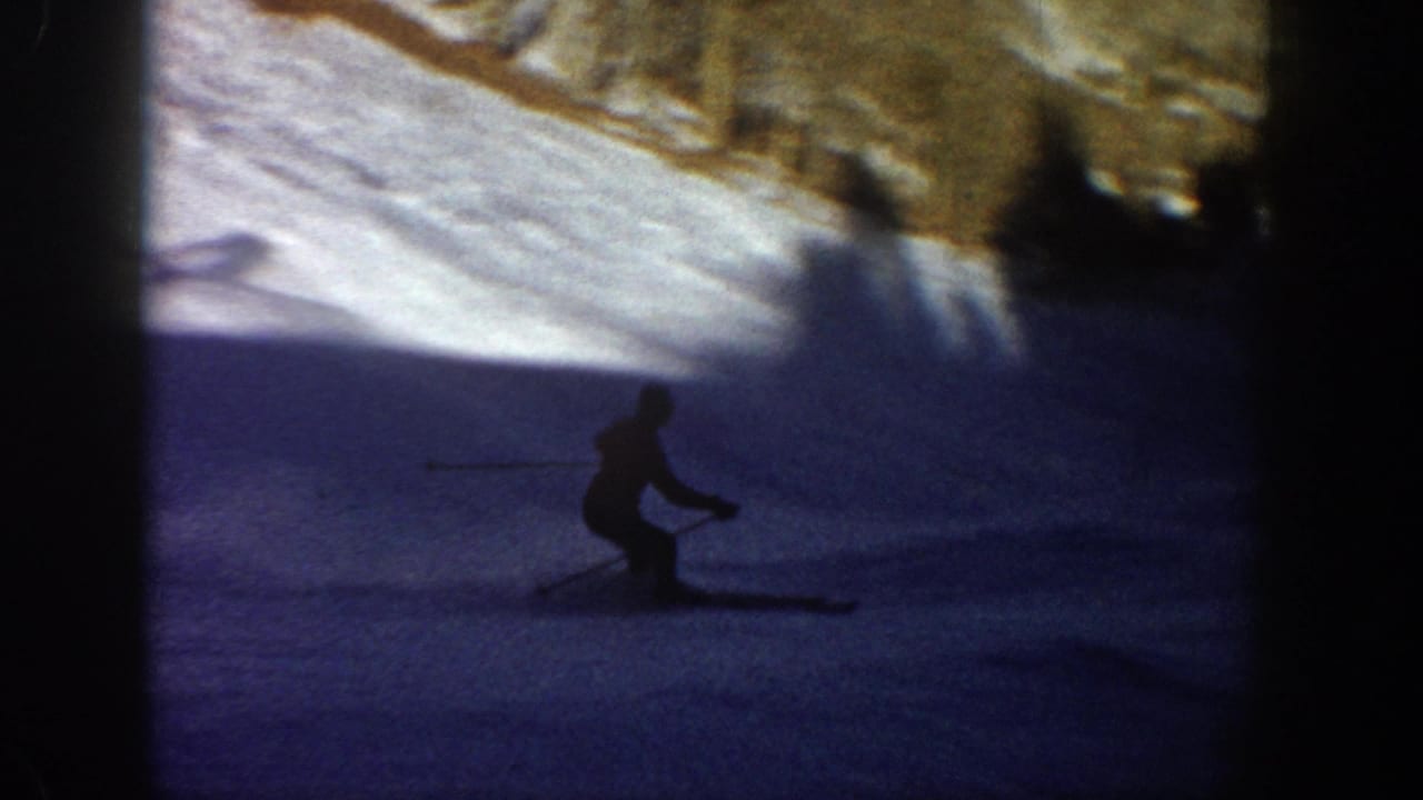 Dark silhouetted skier on a shaded snowfield near a bright upper slope.