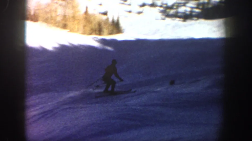 A distant skier continues downhill on a shaded Aspen slope, with pine trees and bright snow visible along the upper edge.