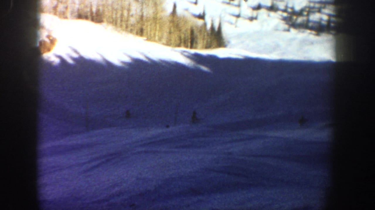 Snowy mountain slope with distant skiers and bright trees at the ridge.