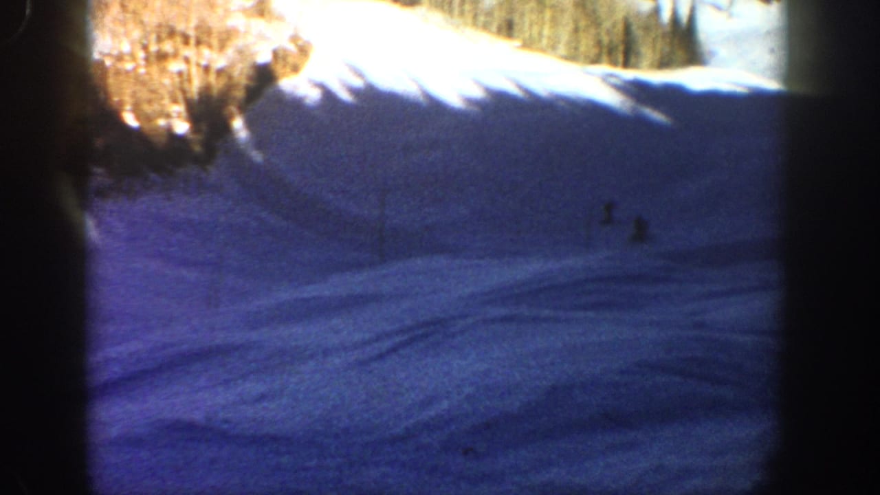 1961 Aspen home-movie frame showing a snowy ski slope with distant skiers and heavy shadow across the snow.
