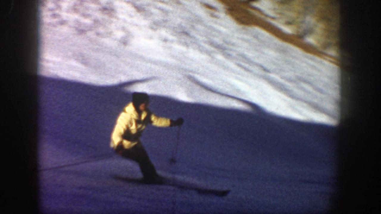 Skier in a yellow jacket descends a snowy slope with poles.