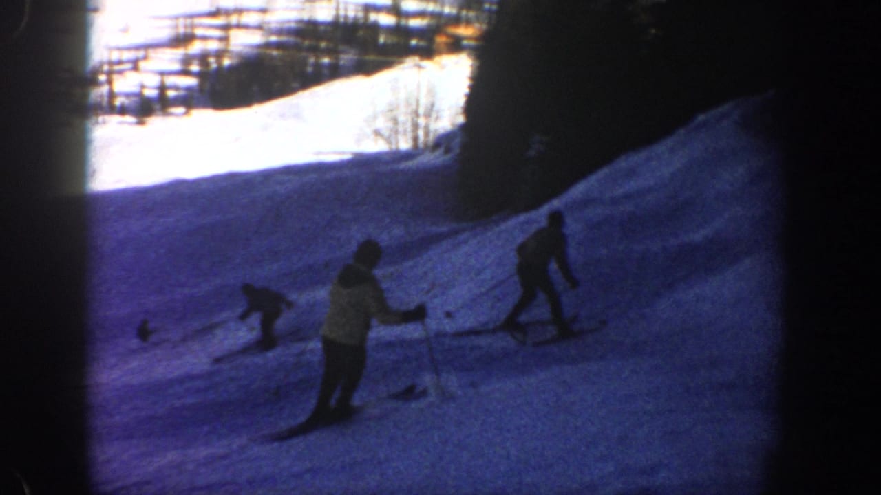 1961 Aspen frame showing multiple skiers on a snowy slope with trees and bright snow in the background.