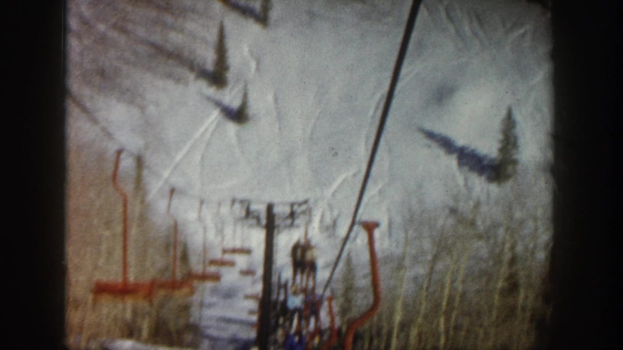 A red chairlift and cable line pass over a snowy Aspen slope, with lift shadows, trees, and a distant seated rider visible.