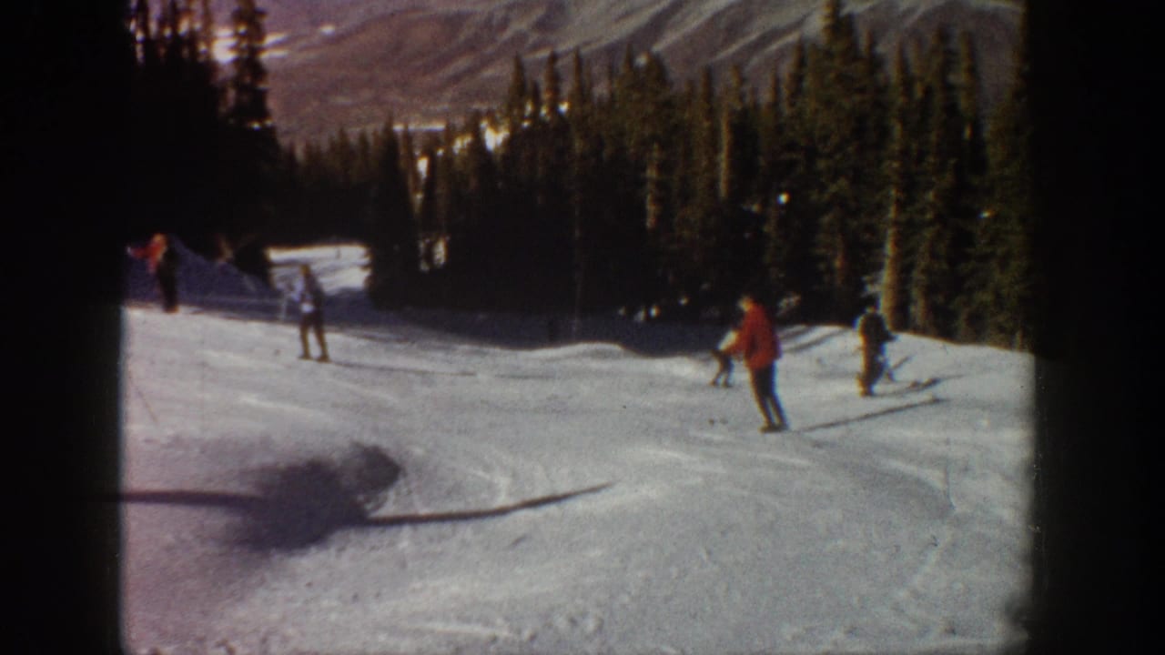1961 Aspen frame showing skiers spaced across a snowy mountain run, with evergreen forest and distant slopes in the background.