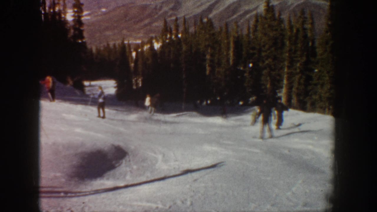 A skier crosses the foreground while others continue down the snowy run.