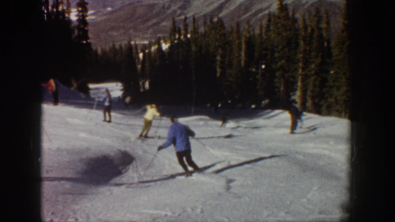 1961 Aspen-area frame with two skiers in the foreground rounding a groomed turn, with more skiers and evergreens behind them.