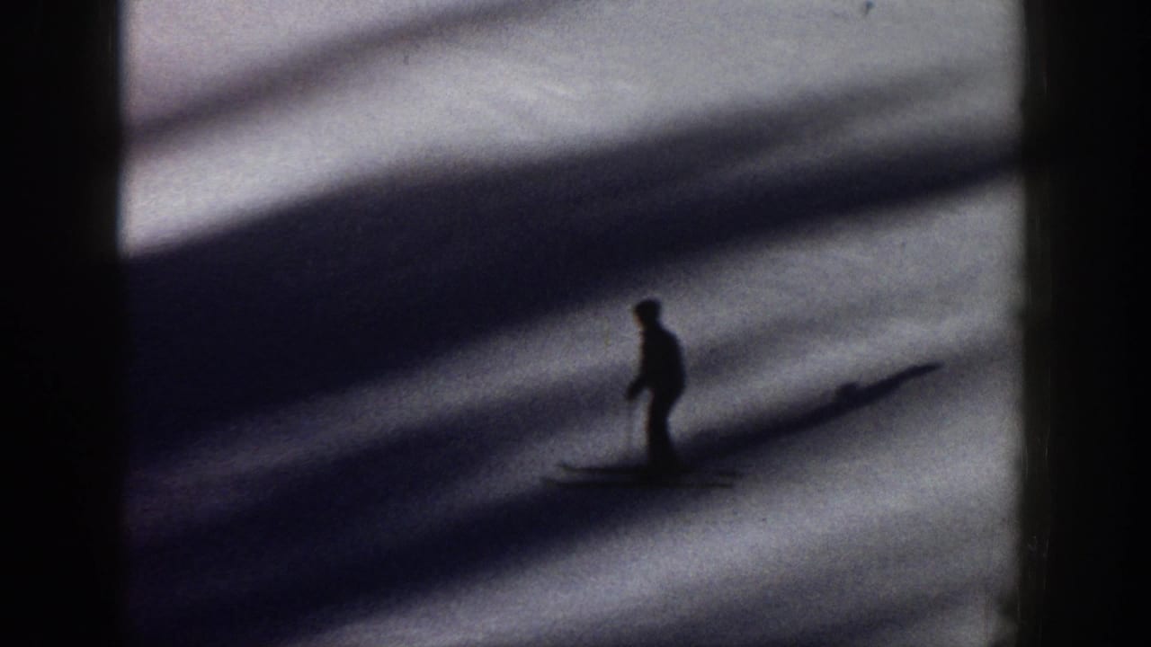 A silhouetted skier moves across shadowed snow in 1961 Aspen home-movie footage, with heavy contrast and soft 8mm grain.