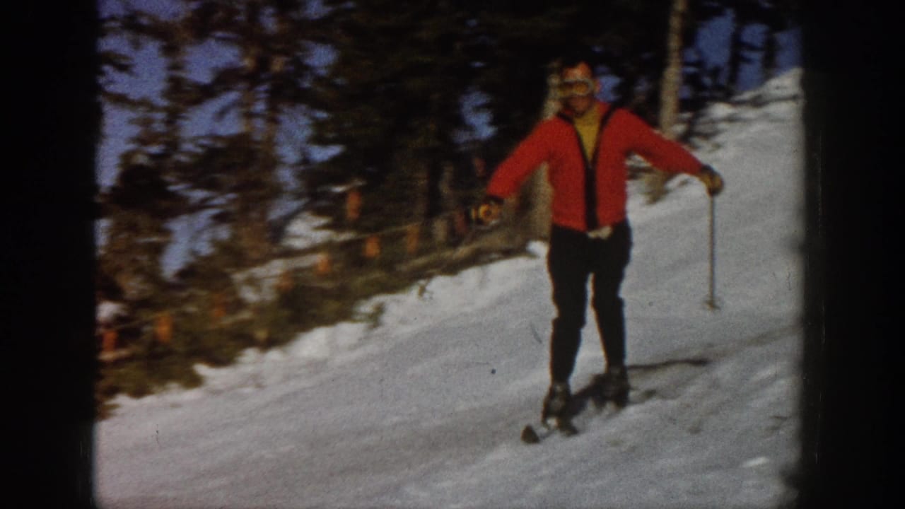 In the supplied 1961 Aspen footage, a skier in a red sweater and goggles approaches on a snowy, tree-lined slope.
