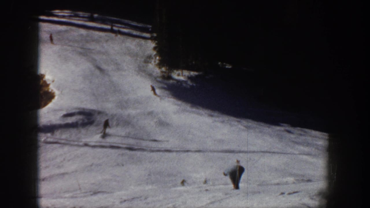 1961 Aspen home-movie frame showing distant skiers on a bright snowy slope with dark evergreen edges.