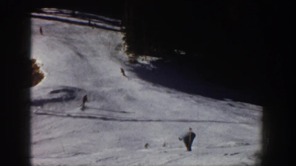 1961 Aspen home-movie frame showing distant skiers on a bright snowy slope with dark evergreen edges.