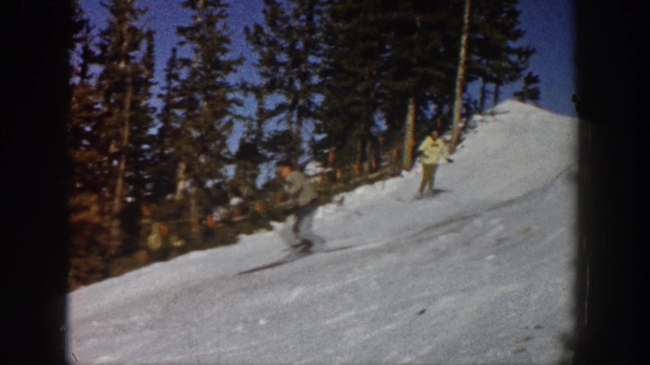 A skier descends a snowy run with trees along the ridge.